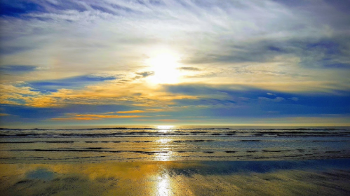 A serene beach scene at sunset, with vibrant colors reflecting on the water and a cloudy sky above.