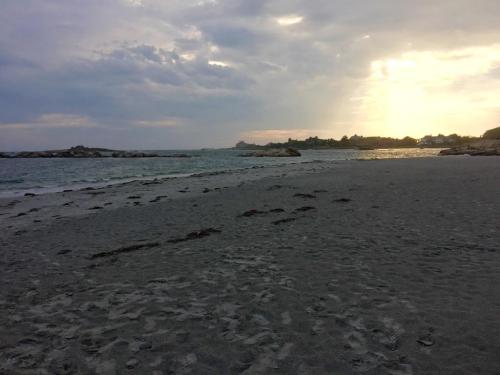 A serene beach at sunset, with gentle waves and a cloudy sky, casting a warm glow over the sandy shore.
