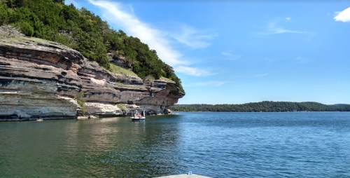 A serene lake scene with rocky cliffs and lush greenery under a clear blue sky.