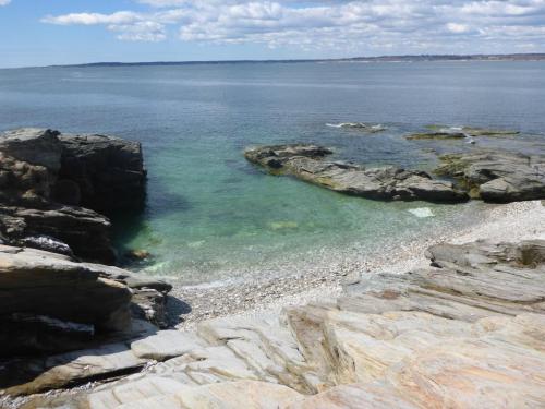 A serene coastal scene featuring clear water, rocky shores, and a cloudy blue sky.