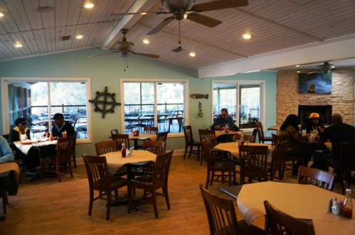 Cozy restaurant interior with wooden tables, fans, and large windows, featuring diners enjoying their meals.