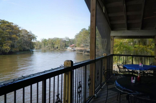 View from a screened porch overlooking a calm river, with trees and a dock in the background. Tables set for dining.