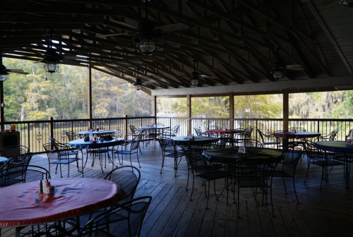 A spacious, covered dining area with round tables and chairs overlooking a serene water view.