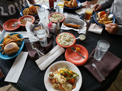 A table set with various dishes, including fried food, salads, and drinks, surrounded by napkins and utensils.