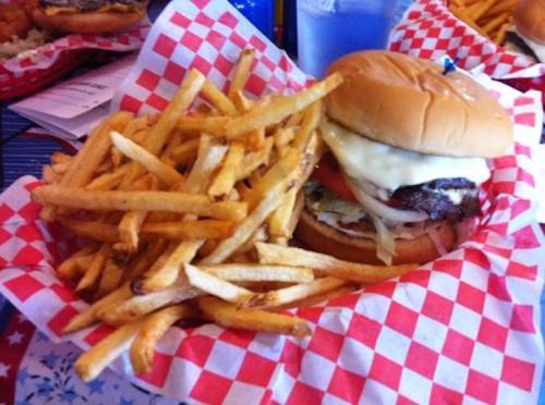 A juicy burger with cheese and toppings served with a side of golden French fries in a red and white checkered basket.