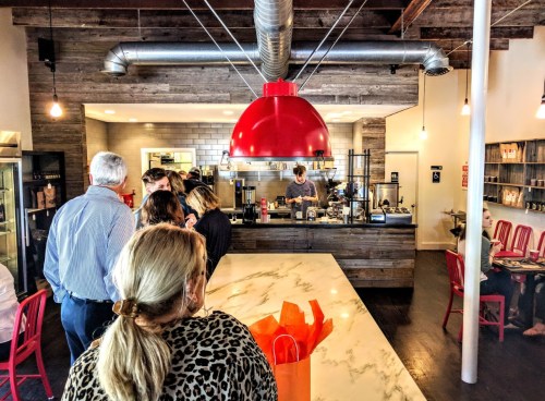 A busy café interior with a red pendant light, a marble counter, and customers waiting in line.