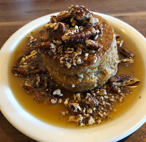 A stack of French toast topped with chopped pecans and drizzled with syrup on a white plate.