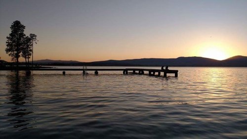 Silhouette of two people on a dock at sunset, with calm water and distant mountains in the background.