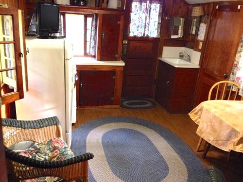 Cozy kitchen with wooden cabinets, a small dining table, and a braided rug, featuring a fridge and sink.