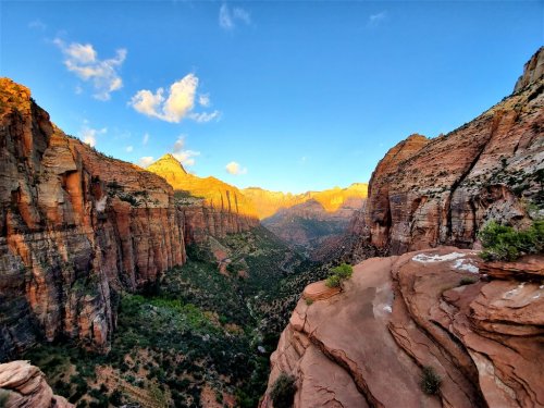 A breathtaking view of Zion Canyon at sunset, showcasing towering cliffs and vibrant colors against a clear blue sky.