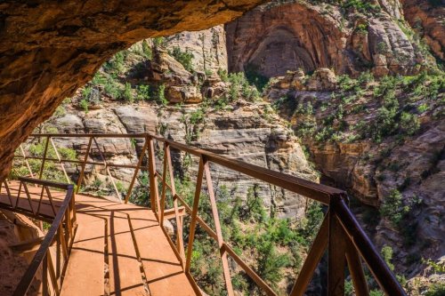 A metal walkway leads through a rocky canyon, surrounded by lush greenery and steep cliffs.