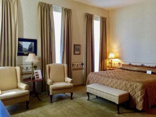 Cozy hotel room with a bed, two armchairs, a bench, and soft lighting from lamps and windows. Elegant decor.