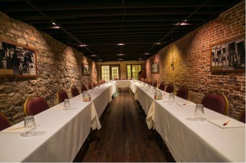A spacious meeting room with long tables, brick walls, and framed photos, set for a conference or event.