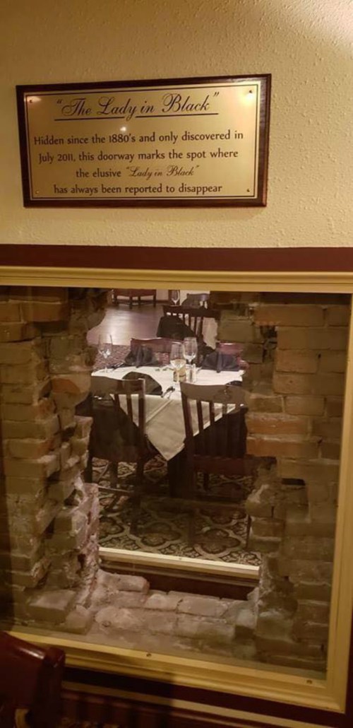 A plaque about "The Lady in Black" next to a bricked-up doorway revealing a dining area behind it.