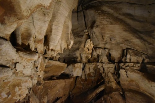 Stalactites and rock formations inside a dimly lit cave, showcasing textured walls and natural geological features.