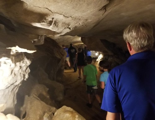 A group of people walking through a dimly lit cave, surrounded by rocky walls and illuminated by soft lights.