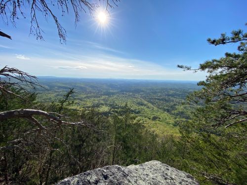 A panoramic view from a rocky overlook, showcasing lush green valleys under a bright sun and clear blue sky.