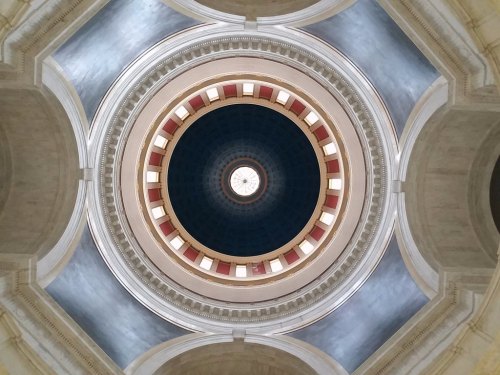 A view of a circular dome ceiling with intricate patterns and a central light fixture, showcasing architectural details.