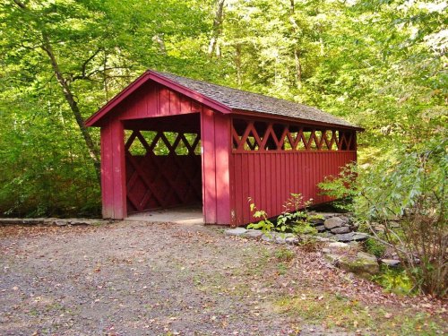 A red covered bridge surrounded by lush green trees and a gravel path.