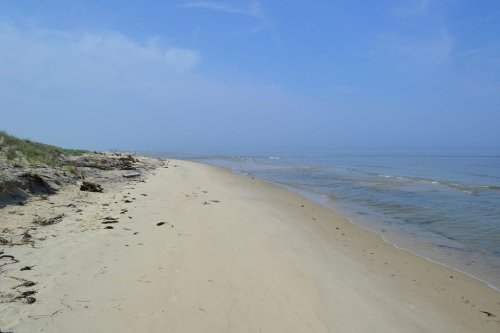 A serene beach scene with soft sand, gentle waves, and a clear blue sky.