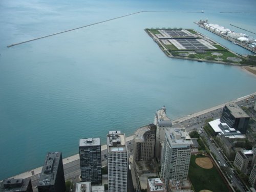 Aerial view of a city shoreline with buildings, a calm lake, and a pier extending into the water.