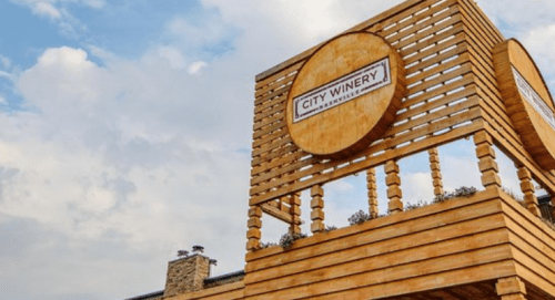 Signage for City Winery on a wooden structure against a cloudy sky.