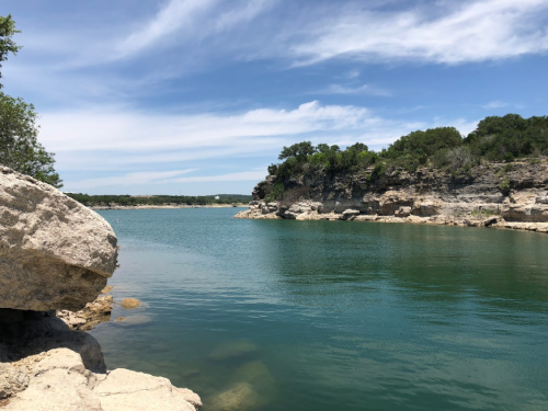 A serene lake surrounded by rocky cliffs and lush greenery under a clear blue sky.