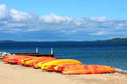 Colorful kayaks in shades of orange and yellow lined up on a sandy beach by a calm blue lake under a cloudy sky.