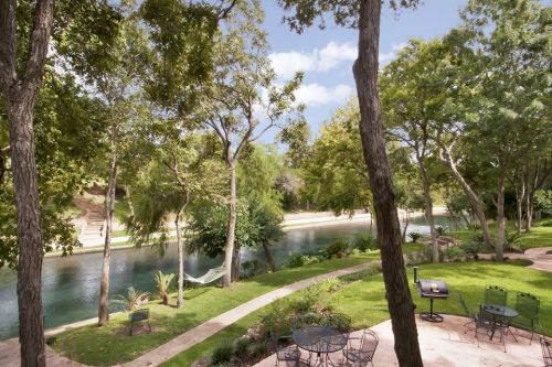 Lush green landscape with a river, trees, and a hammock, creating a serene outdoor setting.