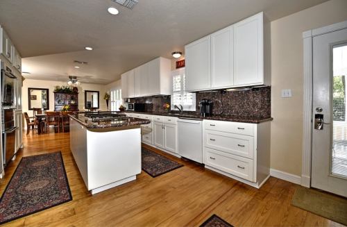 Bright kitchen with white cabinets, granite countertops, and wooden floors, featuring a dining area in the background.