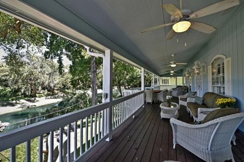 A cozy porch with wicker furniture overlooks a serene river and lush greenery.