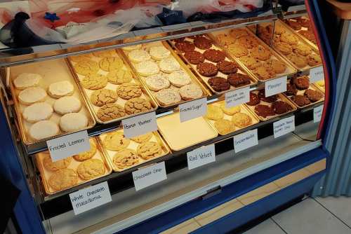A display case filled with various cookies, labeled with flavors like frosted lemon, peanut butter, and red velvet.
