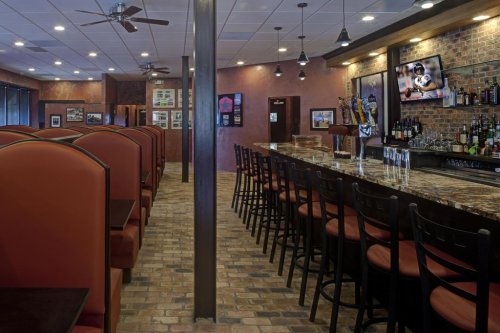 Interior of a restaurant featuring a bar, booths, and a brick wall, with sports memorabilia and a TV on display.