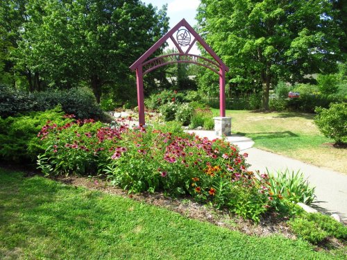 A vibrant garden with colorful flowers and a decorative archway surrounded by lush greenery and a winding path.