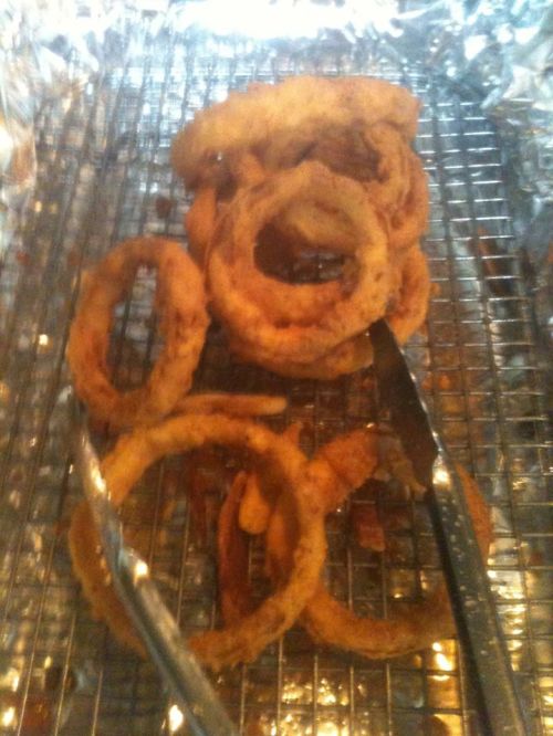 A tray of crispy fried onion rings with tongs resting beside them on a wire rack.