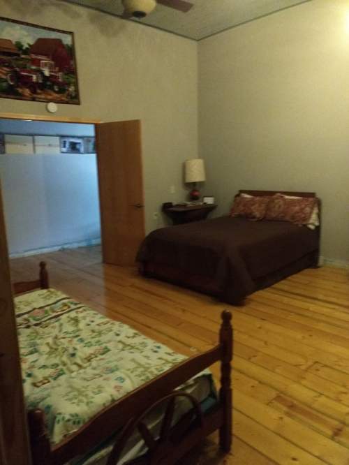 A cozy bedroom with wooden floors, featuring a double bed and a single bed, along with a lamp and wall art.