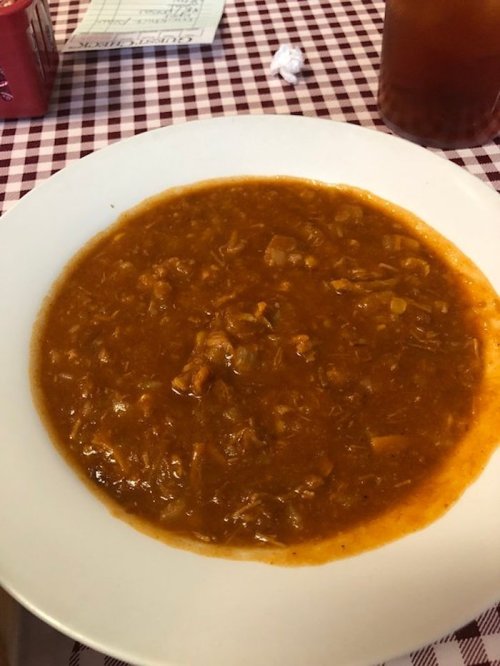 A plate of thick, brown stew with shredded meat and vegetables, served on a white dish against a checkered tablecloth.