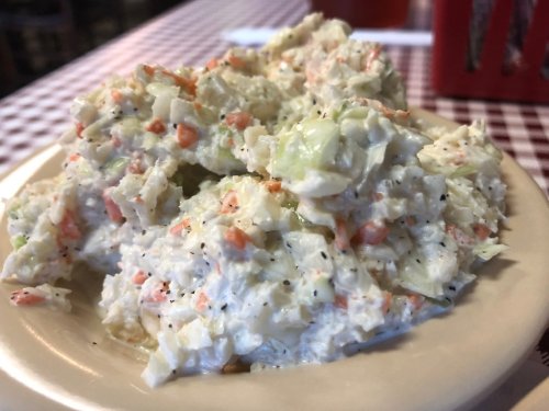 A serving of creamy coleslaw with shredded cabbage, carrots, and a peppery seasoning on a plate.