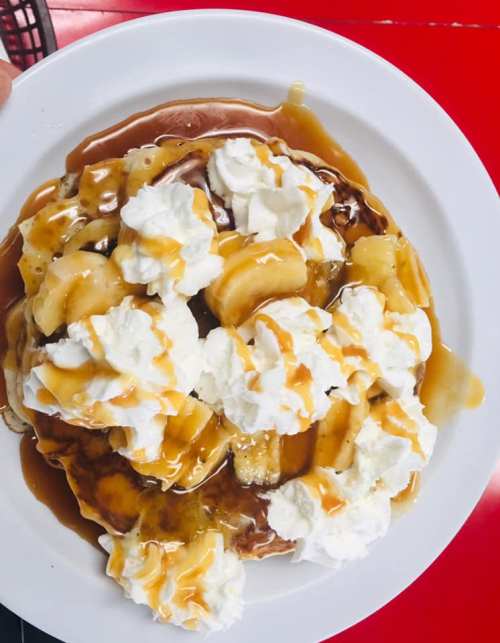 A plate of pancakes topped with sliced bananas, whipped cream, and drizzled with caramel sauce.