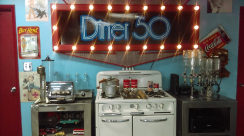 Retro diner setup featuring a vintage stove, decor, and a glowing "Diner 50" sign against a blue wall.