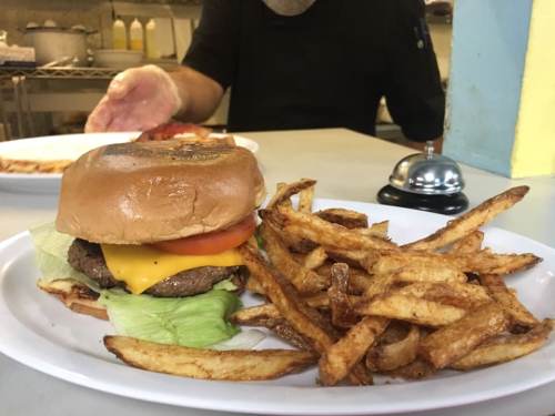 A cheeseburger with lettuce and tomato on a plate, accompanied by a side of golden fries and a small bell.
