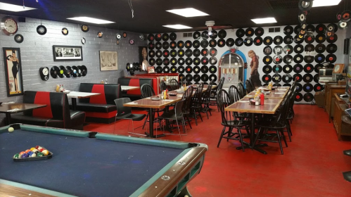 A retro diner with a pool table, red flooring, and walls decorated with vinyl records and vintage photos.