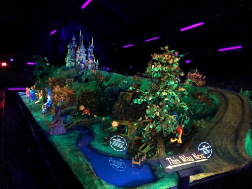 A colorful miniature scene featuring a castle, trees, and characters, illuminated under purple lights.