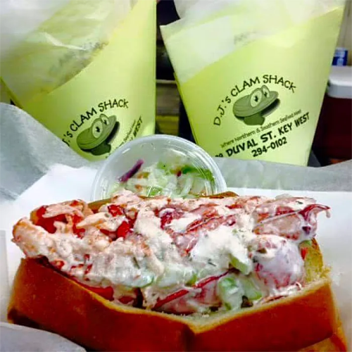 A lobster roll with creamy filling on a bun, served with a side of coleslaw and yellow takeout containers in the background.