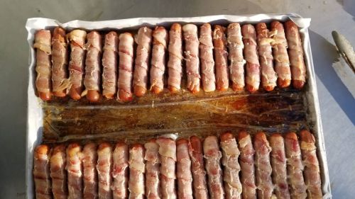 A tray of bacon-wrapped hot dogs arranged neatly, with some grease visible on the surface.