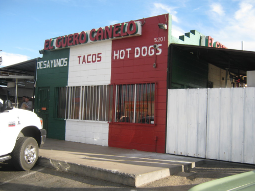 Exterior of El Guero Canelo, a colorful restaurant featuring tacos and hot dogs, with a red, white, and green facade.