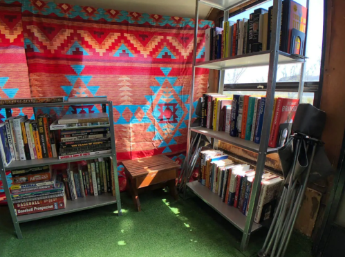 A cozy reading nook with colorful patterned fabric, two metal bookshelves filled with books, and a small wooden bench.
