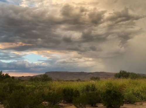 A dramatic sky filled with clouds over a landscape of green shrubs and distant mountains.