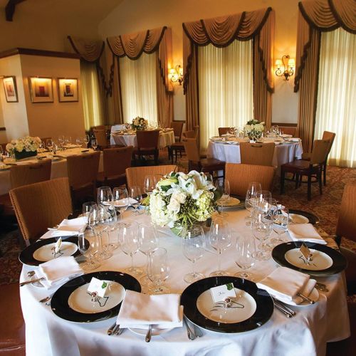 Elegant dining room set for a formal meal, featuring round tables with white tablecloths and floral centerpieces.