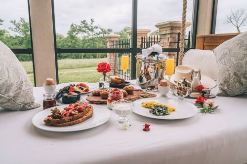 A beautifully arranged breakfast spread on a table, featuring fruits, pastries, and an omelet, with a scenic view outside.